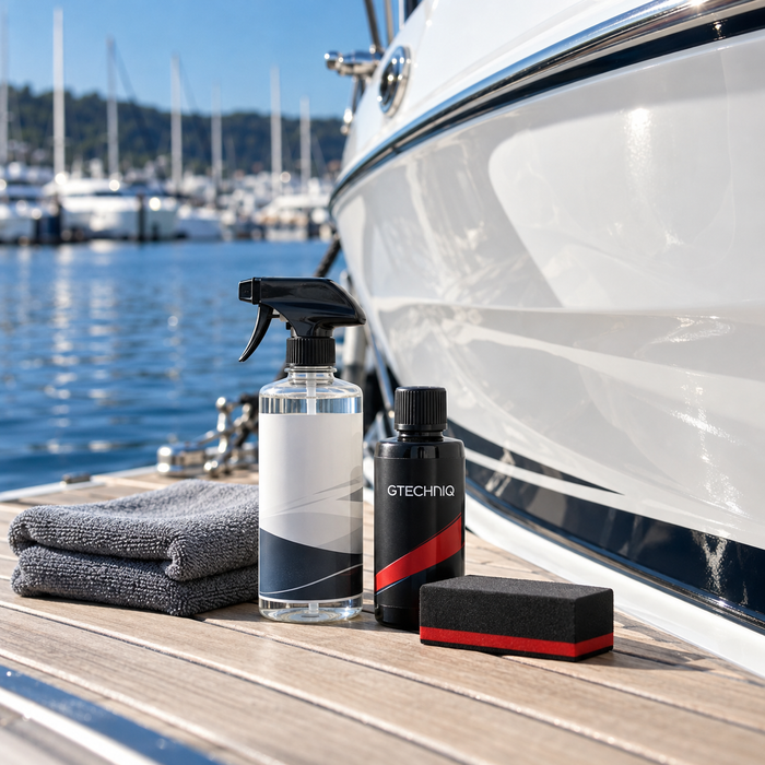 Gtechniq branded bottle with a preparation spray, microfiber towels and coating applicator beside a white boat hull.