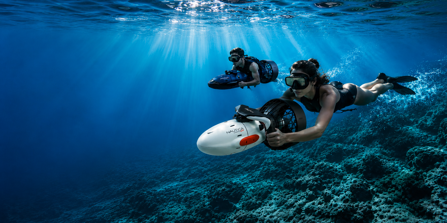An underwater scene showing two divers swimming above a coral reef, with one diver holding a white and black robotic underwater camera.
